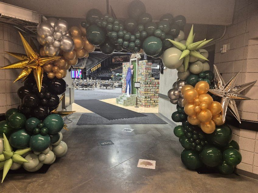 Balloon archway in green, gold, and silver colors, decorated with starburst shapes, framing an interior doorway.
