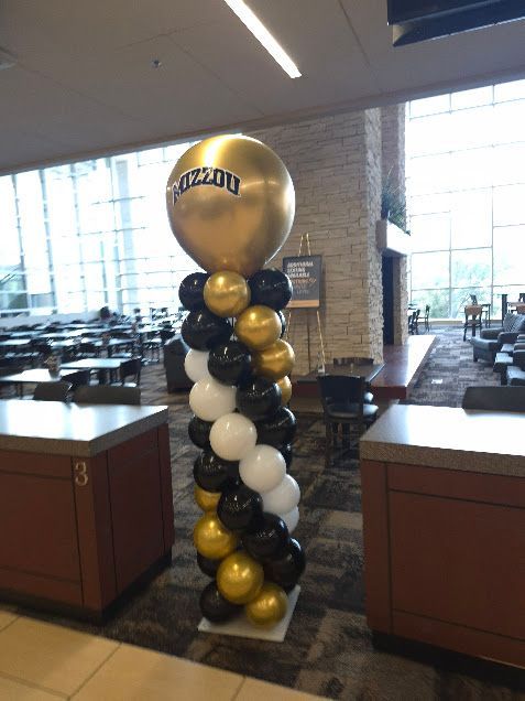 Balloon column with gold, black, and white balloons, topped with a large gold balloon with 