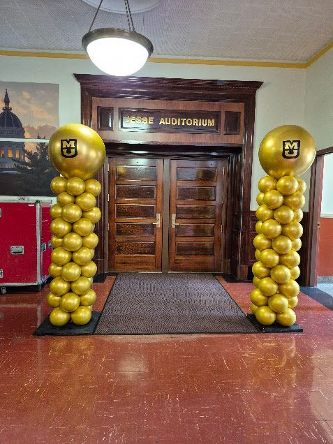 Two golden balloon columns flank the entrance to 