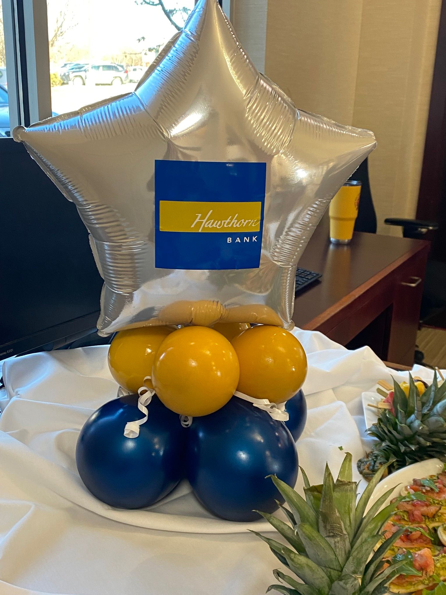 A star shaped balloon is surrounded by blue and yellow balloons on a table.