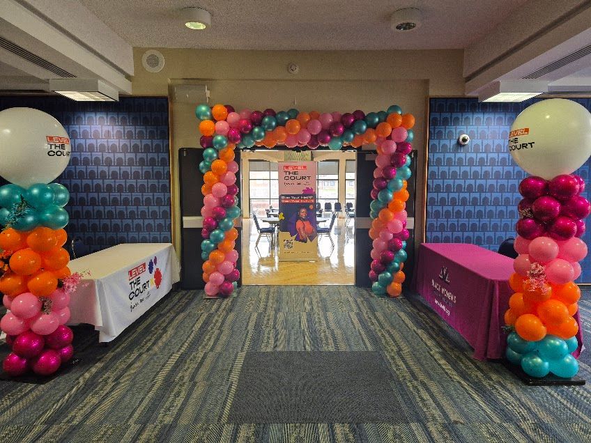 Entrance decorated with balloon columns and arch for an event. Tables are set up, event information displayed in the doorway.
