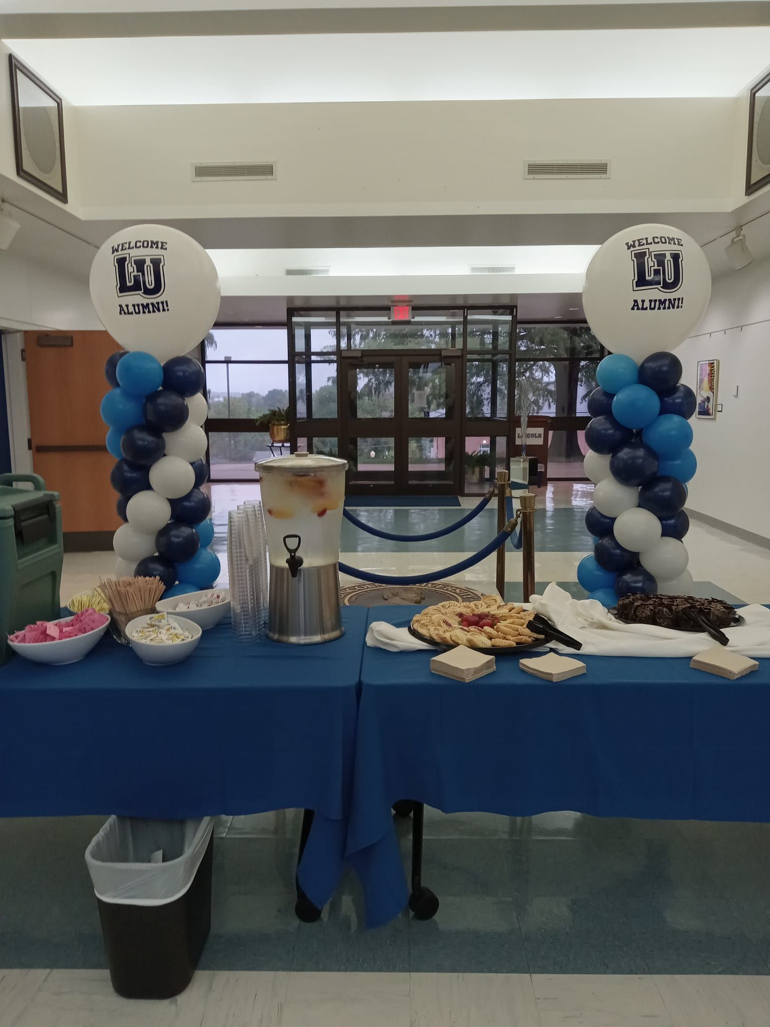 A buffet table with blue and white balloons in a hallway
