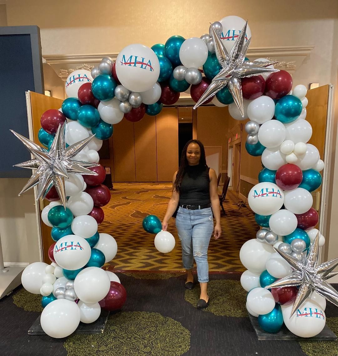 A woman is walking through an arch of balloons with letters aaa on them