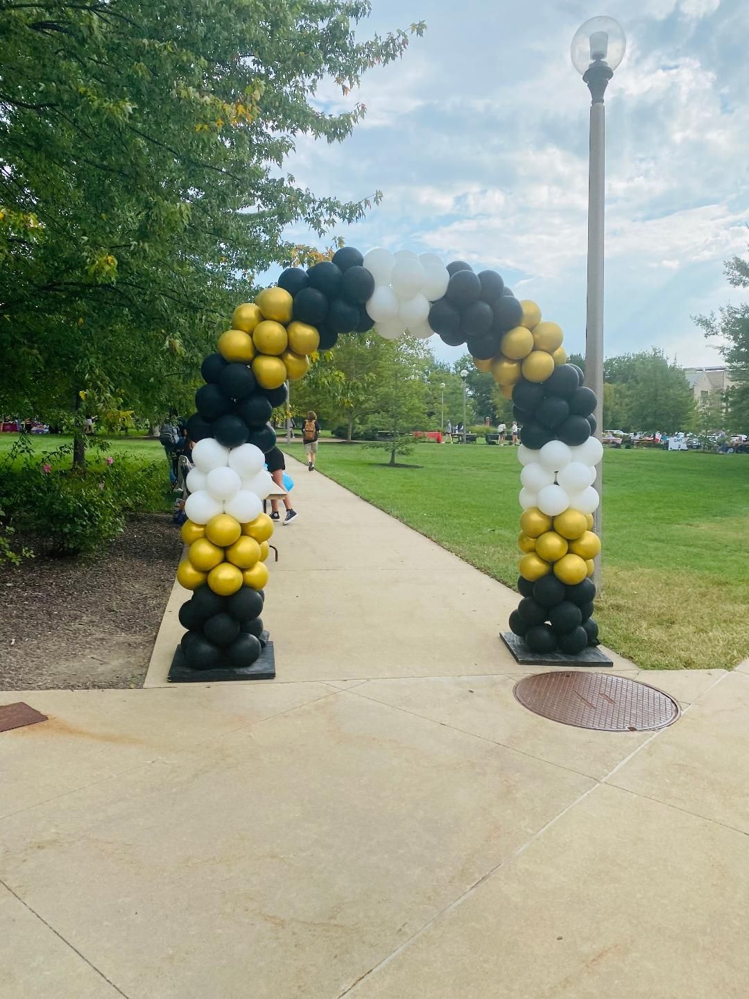 A black and gold balloon arch in a park