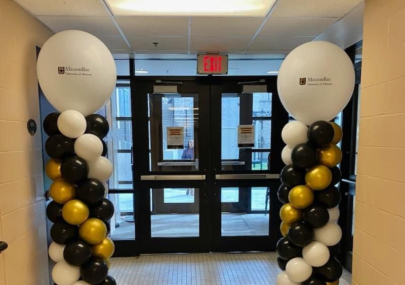 A hallway with two columns of black and gold balloons