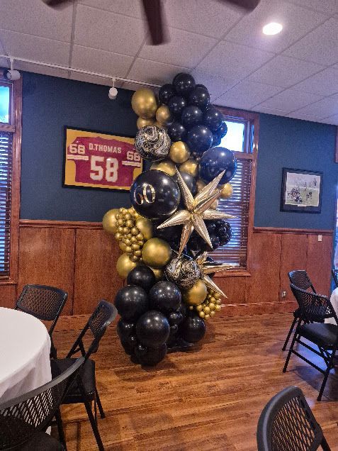 Black, gold, and silver balloon arch with starburst accents in a room with dark wood paneling.