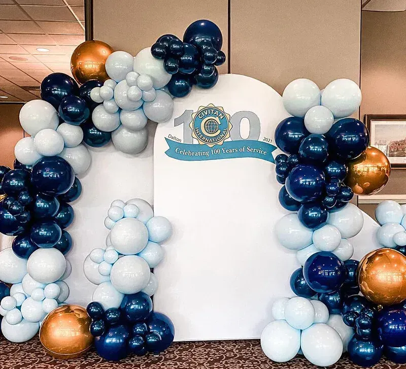 A white sign with blue and gold balloons surrounding it.