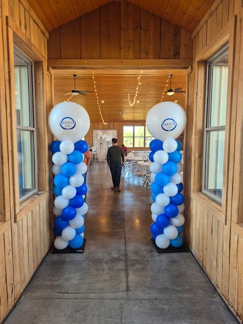 Entrance decorated with blue and white balloon columns. Person walks towards a room with tables.