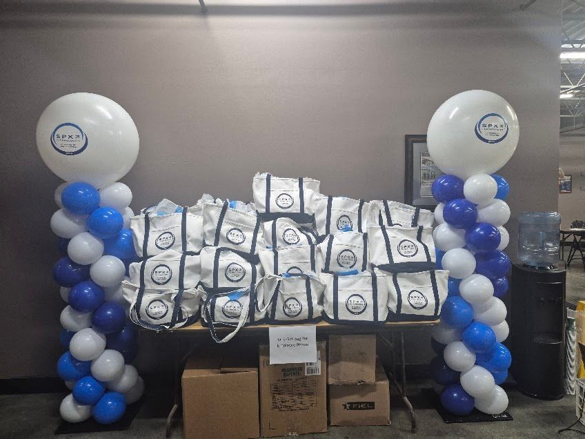 Table with branded gift bags between two balloon columns in a warehouse.