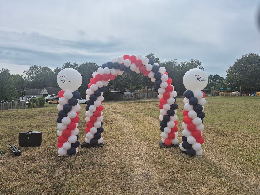 Balloon archway with red, white, and blue balloons, set in a grassy field.