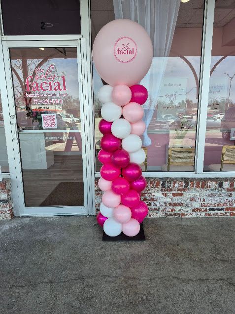 Pink and white balloon column outside a business entrance with a large pink balloon on top.