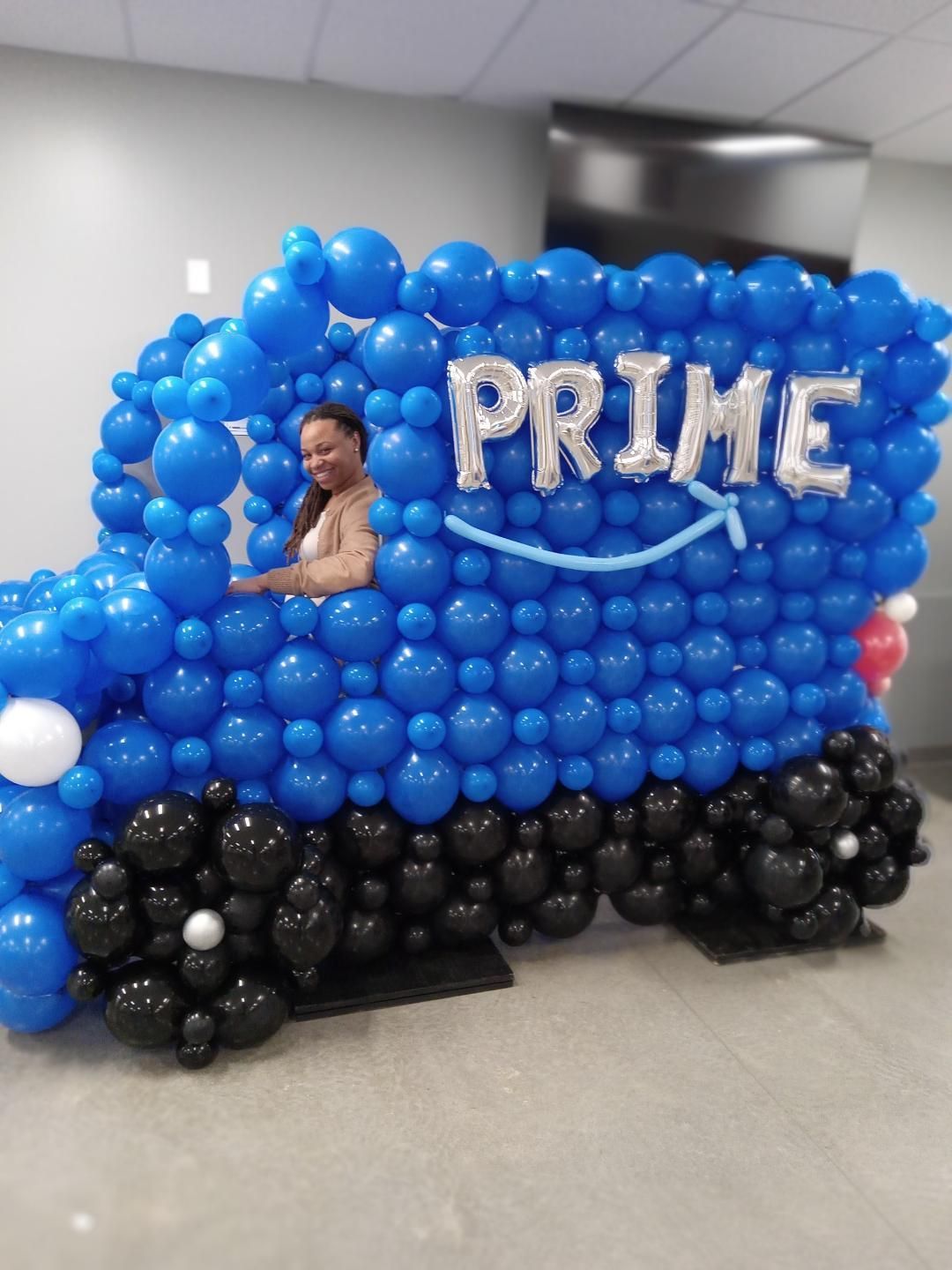 A woman is standing in front of a truck made of balloons that says prime