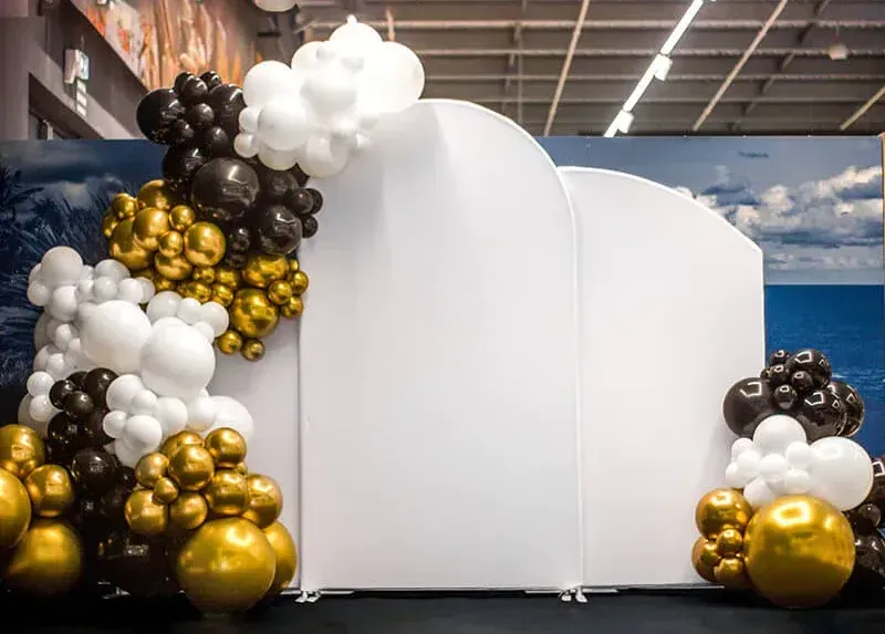 A white wall surrounded by black , white and gold balloons.