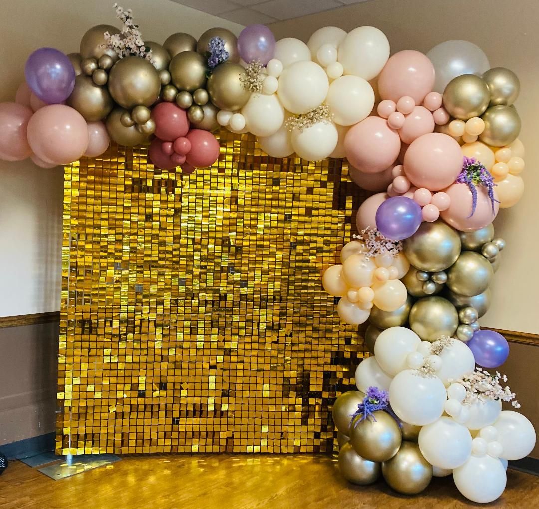A gold wall covered in balloons and flowers in a room.