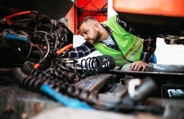 A man in a green vest is working on the underside of a semi truck – Indianapolis, IN - Midwest Logistics & Roadside Repair