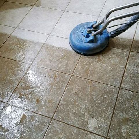 A blue floor-cleaning machine on a tiled kitchen floor with cabinets and a dishwasher nearby