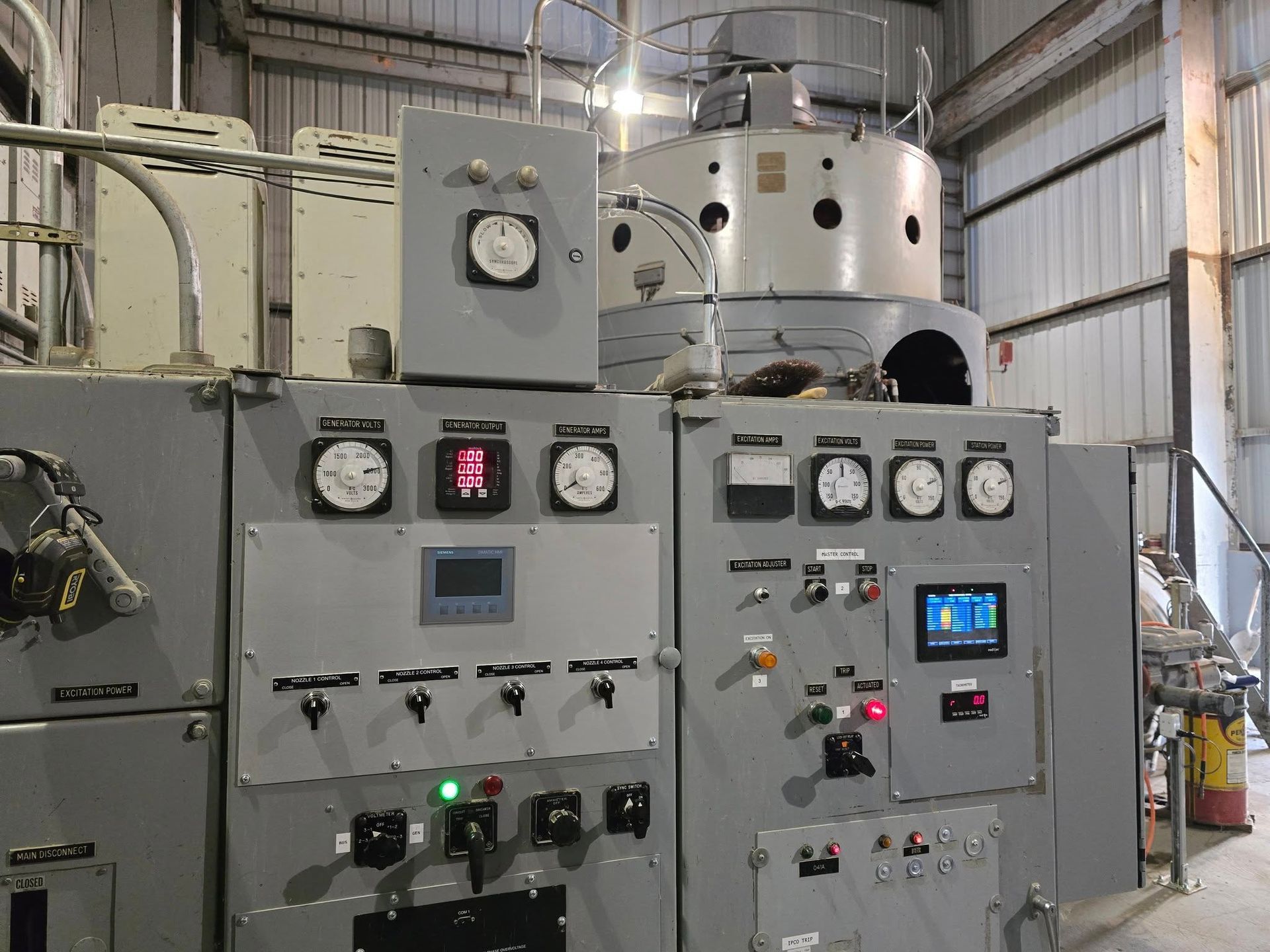 Control panel with gauges, switches, and a digital screen in an industrial setting.