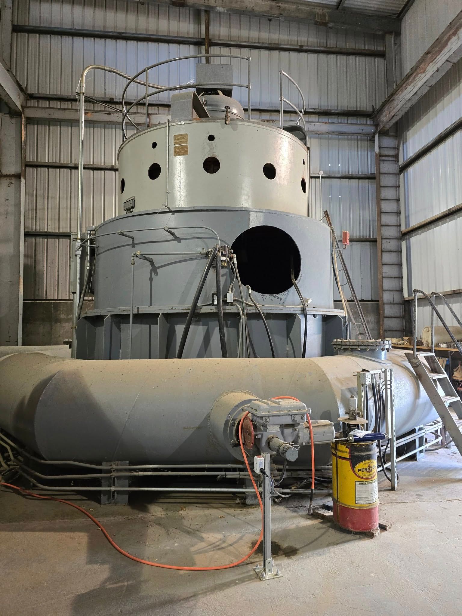 Large industrial water pump inside a metal building, painted gray and white, with connected pipes and a red fire extinguisher.