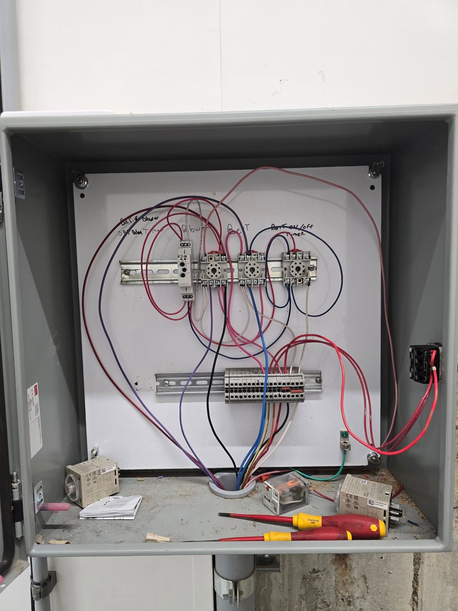 Open electrical control box with wiring, terminal blocks, and tools.
