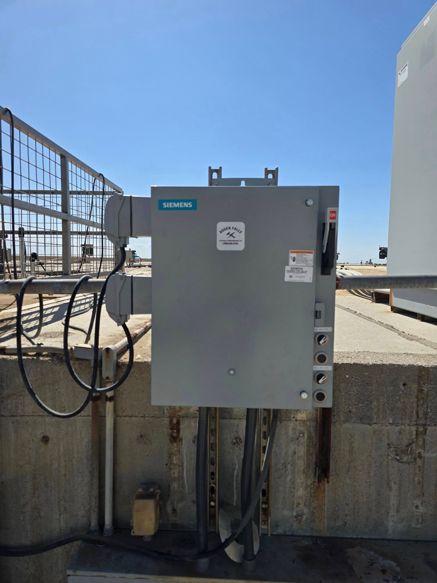 Gray electrical box on a concrete structure with wiring and a blue sky in the background.