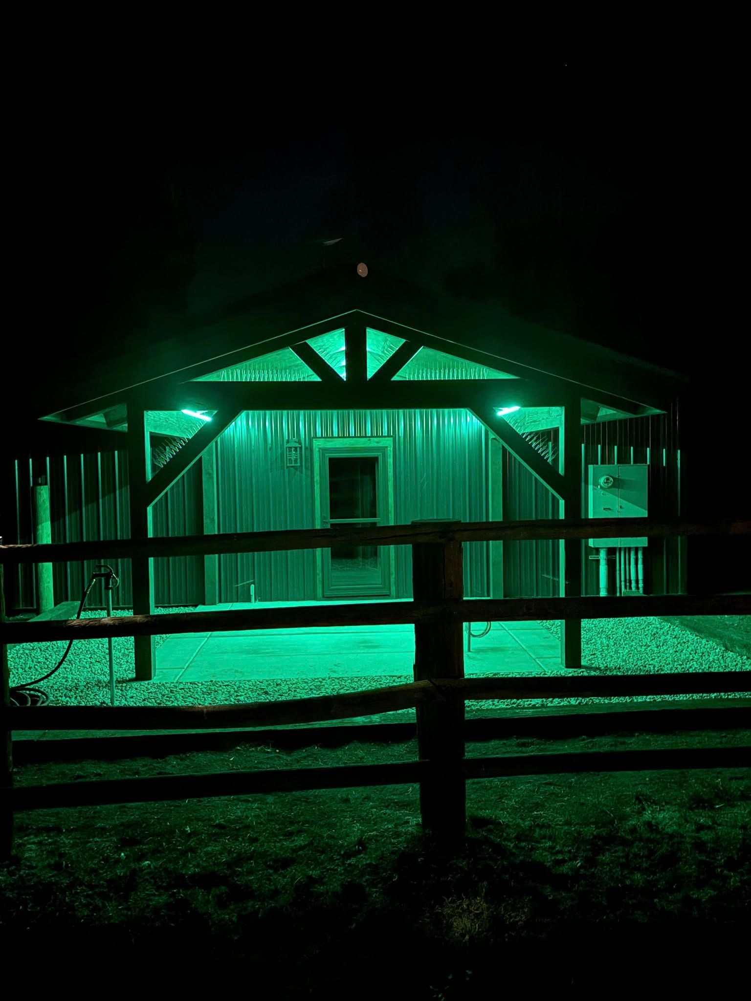 Green-lit wooden structure behind a wooden fence at night.
