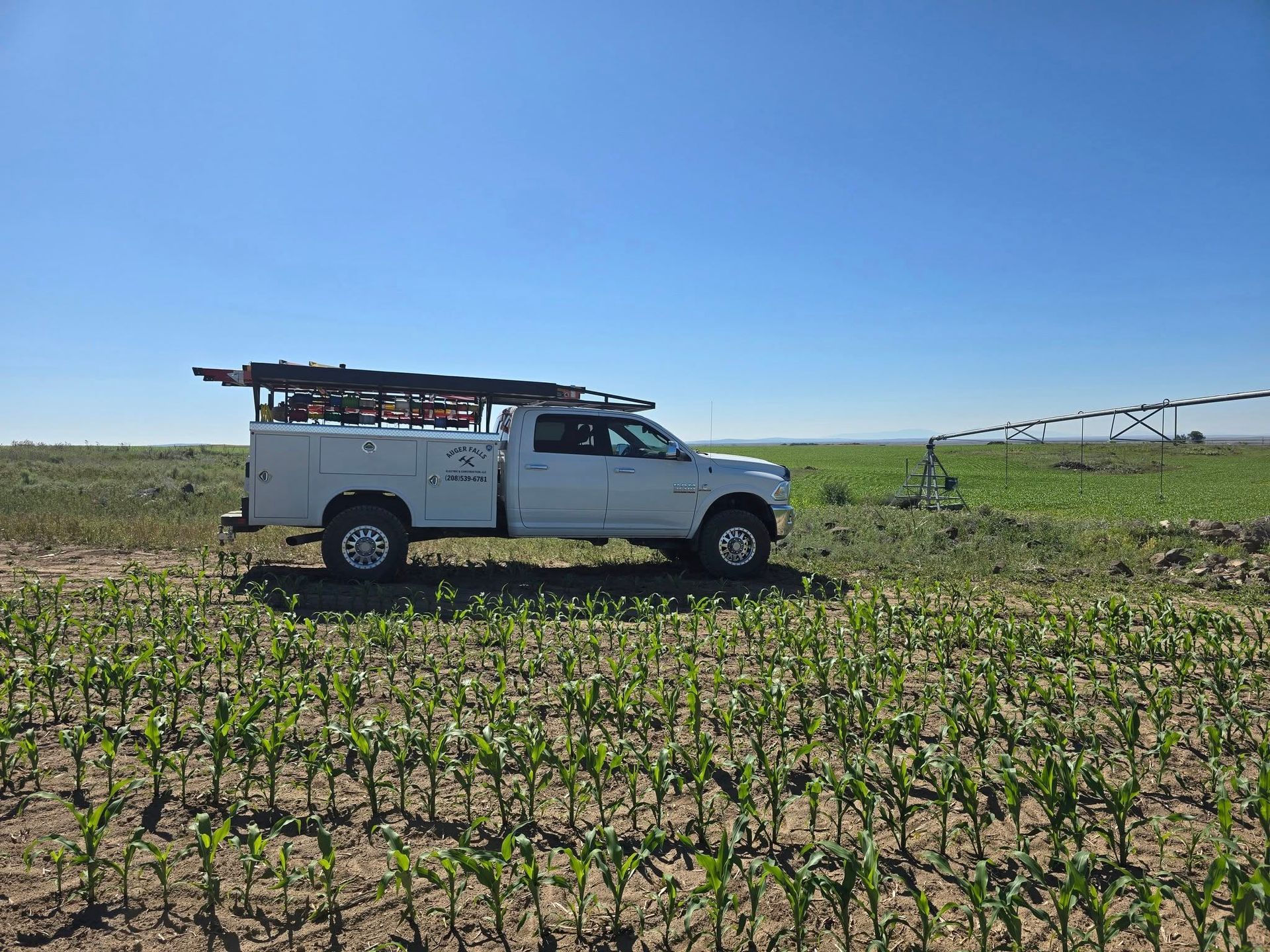 White truck in a field, likely for agriculture, with a sprinkler system in the background, under a bright blue sky.