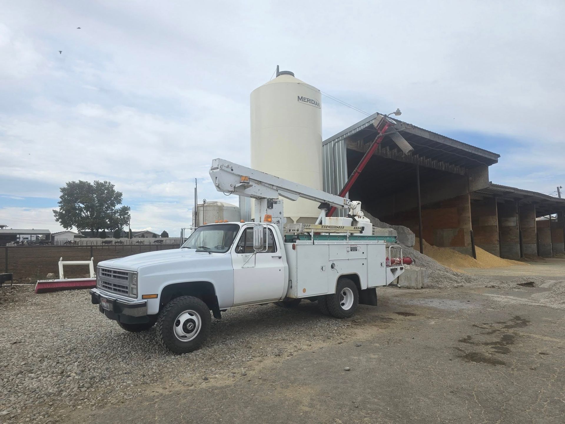 White utility truck with an aerial lift next to a grain silo and barn.