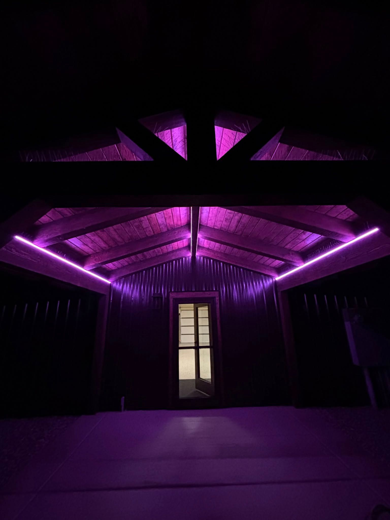 A wooden structure with purple LED lights on the roof. The open doorway has a light.