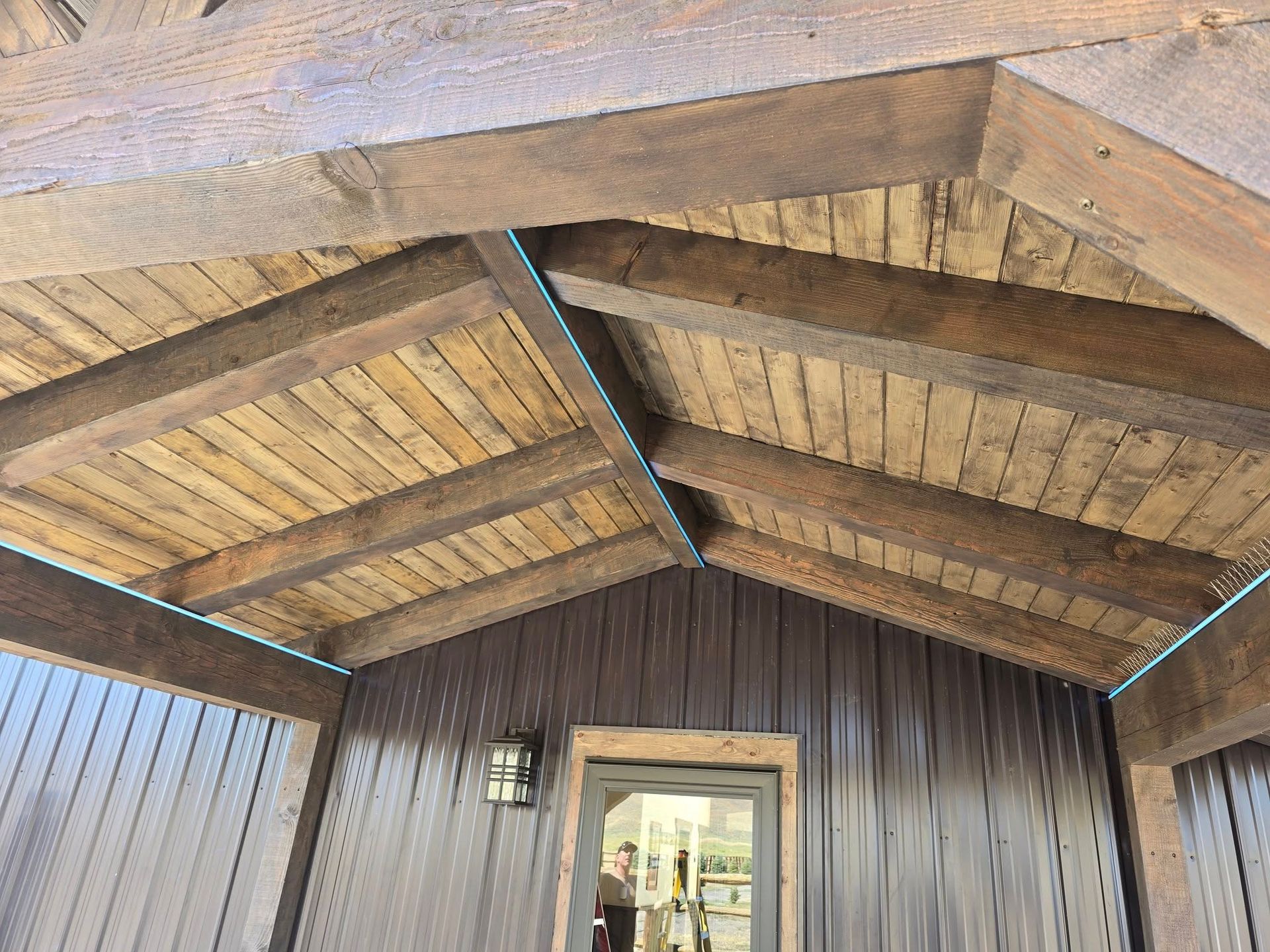 Wooden beams and planks forming a rustic ceiling over a dark brown building entrance.