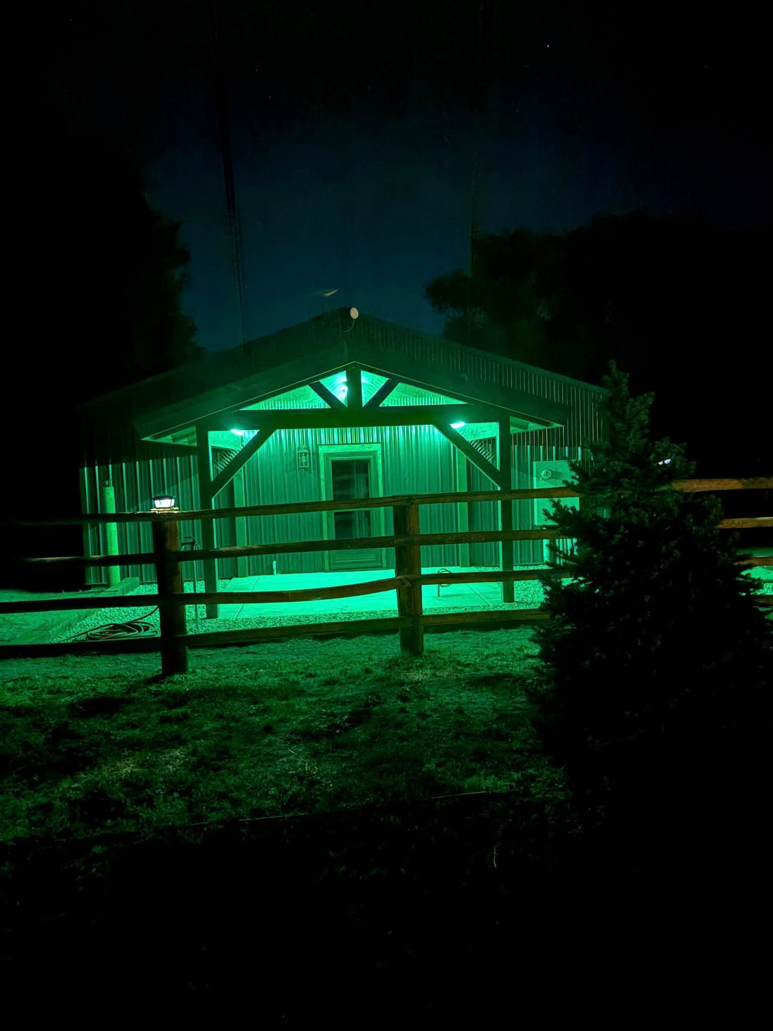 Green-lit wooden shed at night, with a fence.