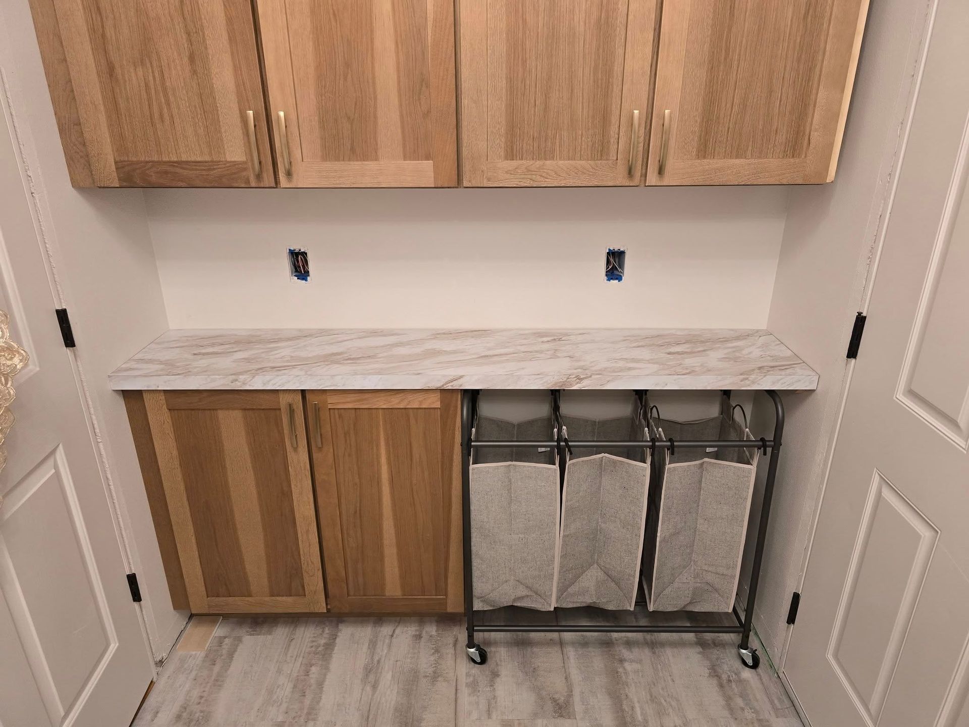 Laundry room with light wood cabinets, white walls, and a multi-compartment laundry hamper.