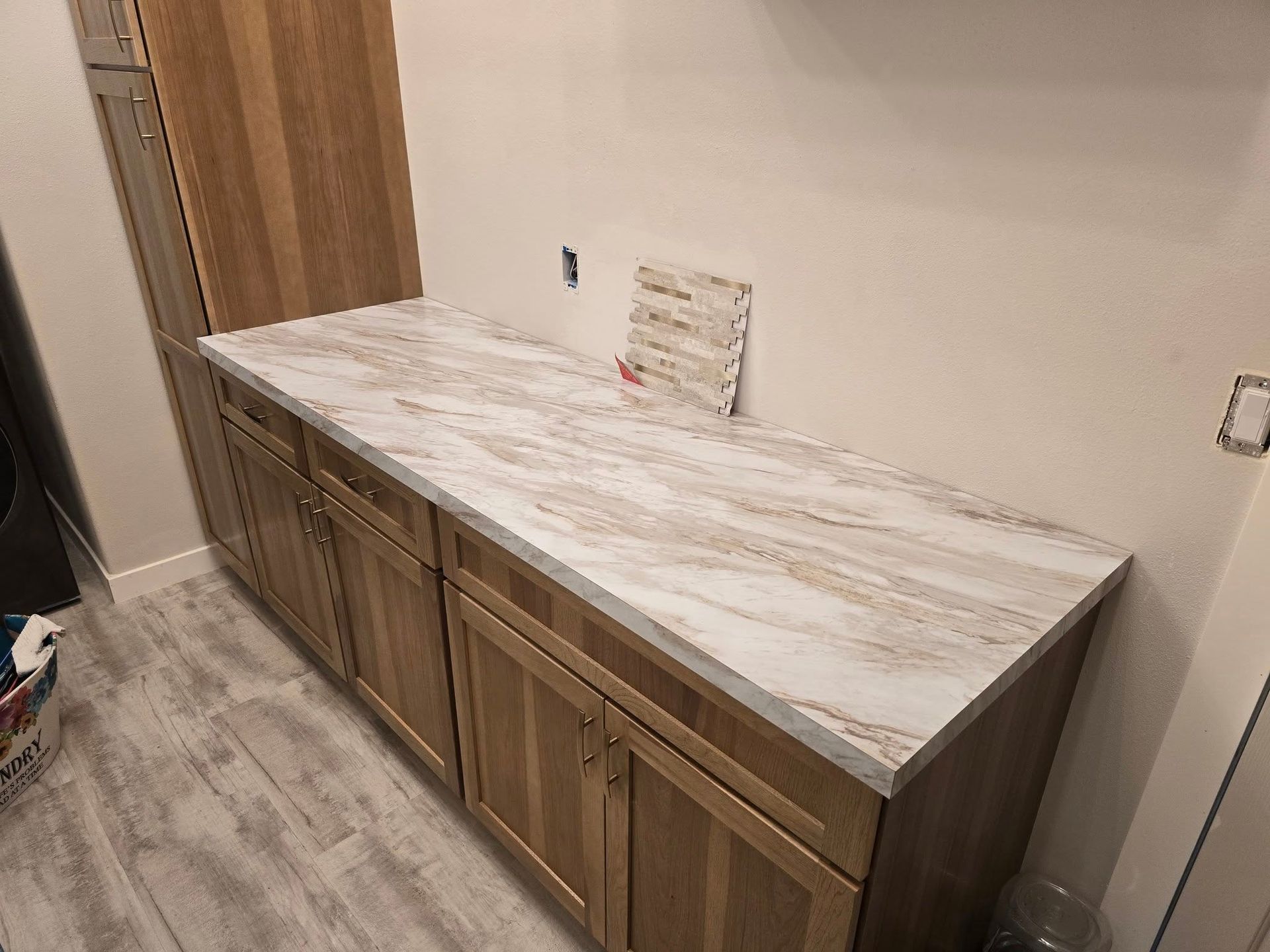 Wooden cabinets with a marble countertop, against a light wall, and a wood-tone cabinet.