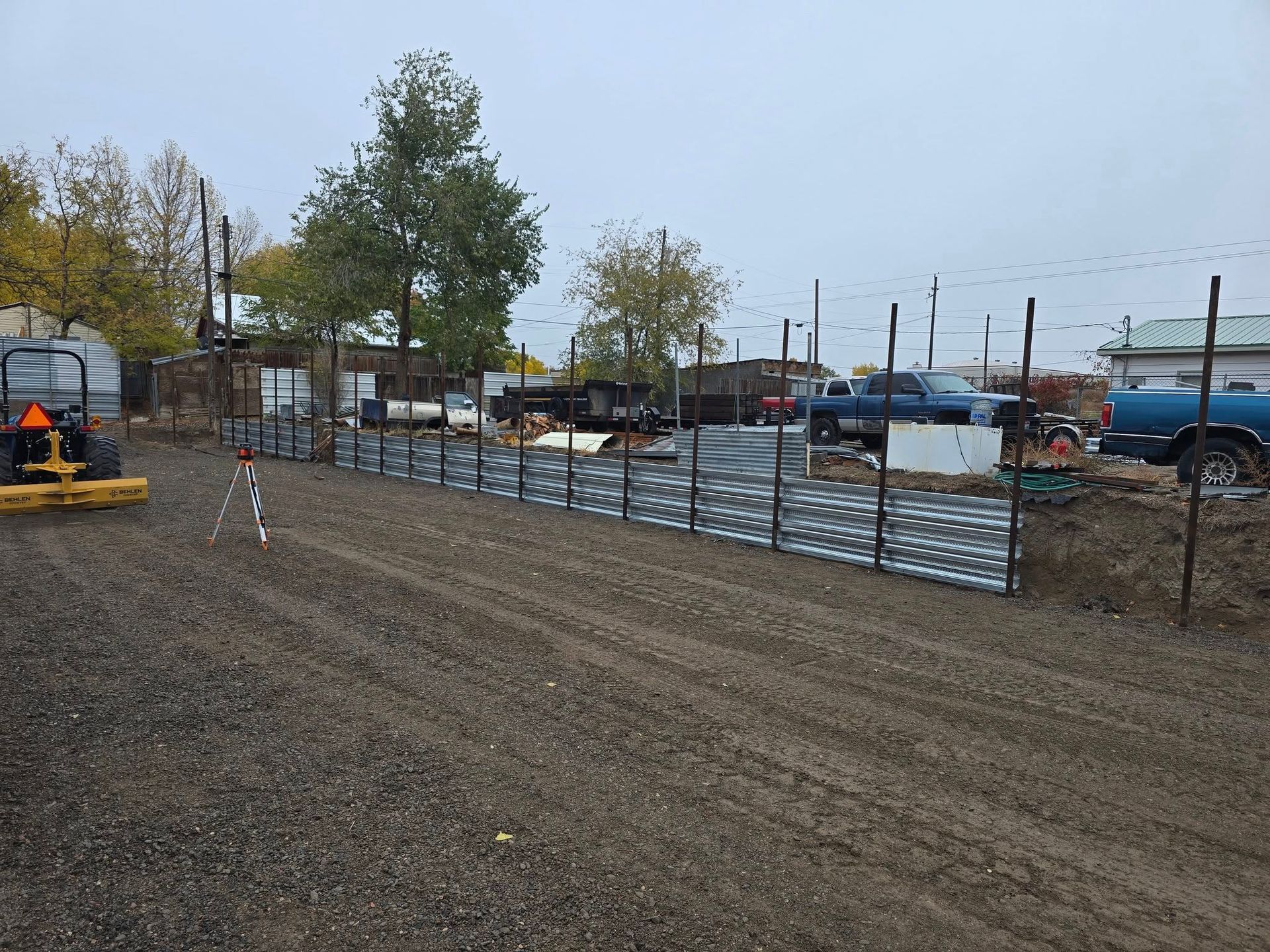 Construction site with metal fence, gravel ground, and parked vehicles.