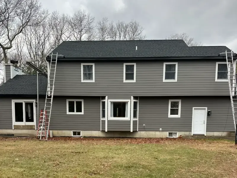 Gray house with dark roof and white window frames; two ladders propped against the roof.