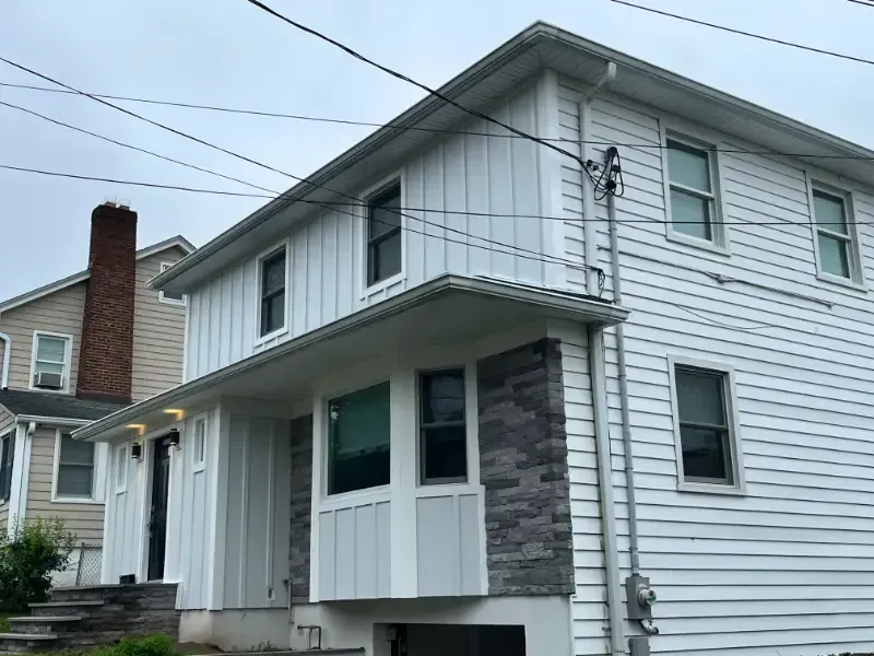Two-story white house with gray stone accents and power lines overhead.