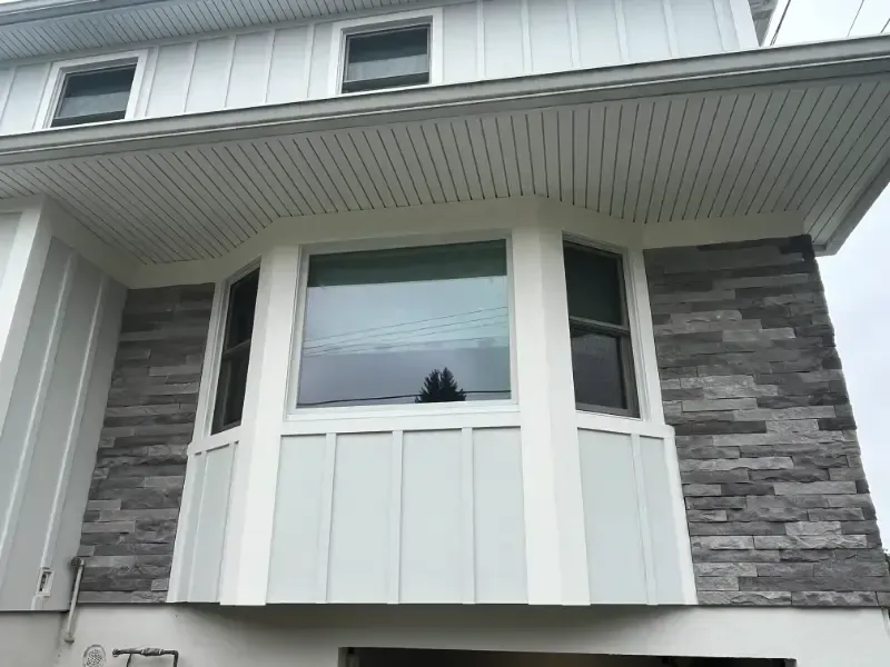 Exterior of a house with gray stone and white siding around a large bay window.