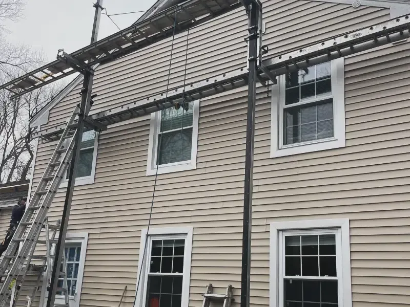 Scaffolding attached to a two-story beige house with multiple windows, used for exterior work.