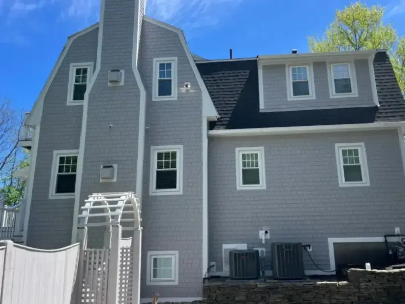 Gray house with white trim and black roof under a blue sky.