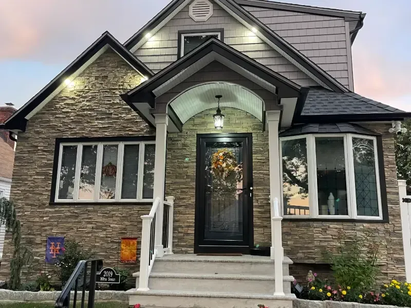 House exterior with stone facade, dark door, and porch. White trim, black roof, and windows.
