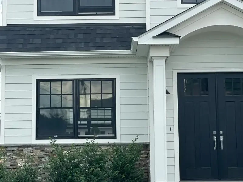 Exterior of a house with light blue siding, black window frames, and a dark blue front door.
