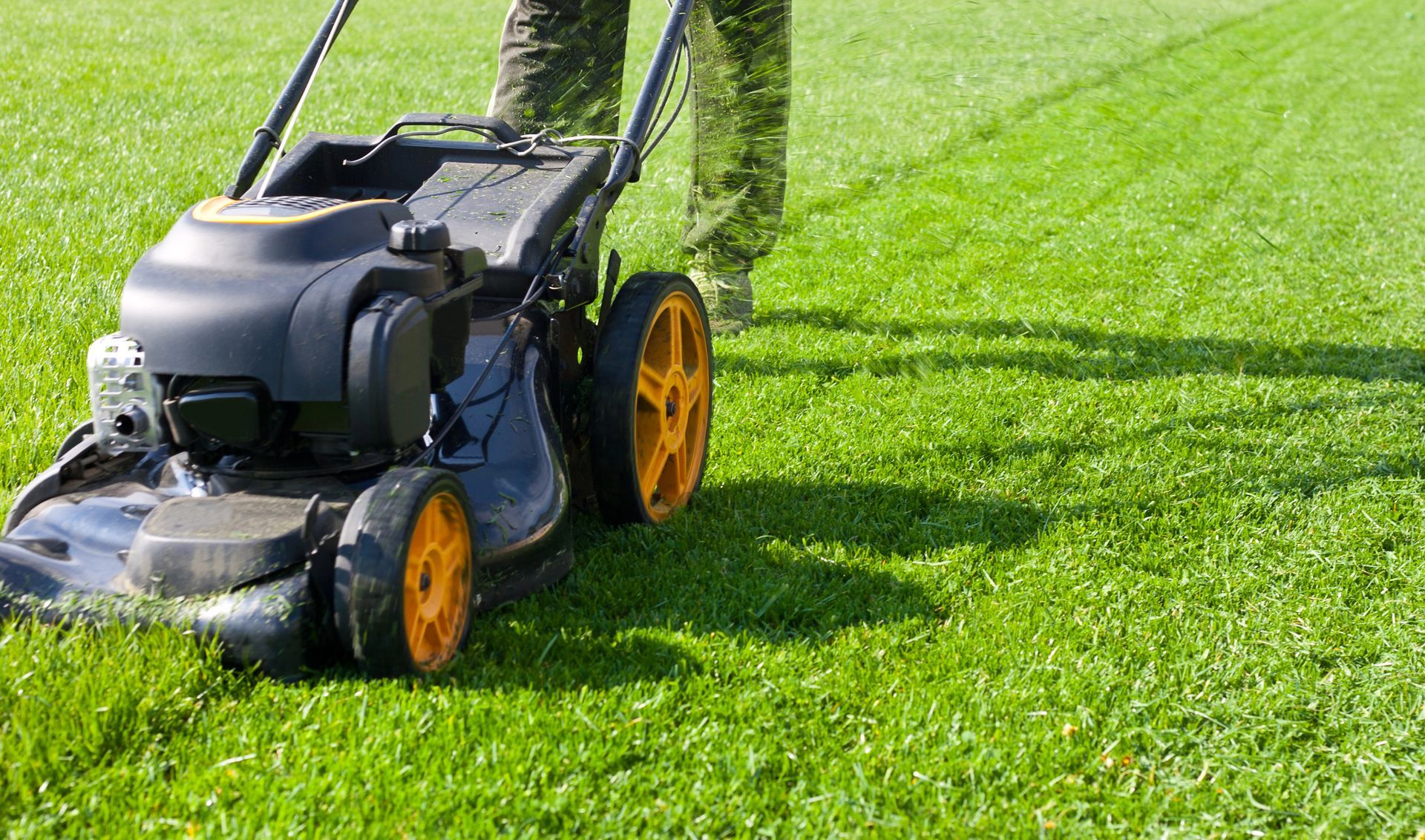 A person is mowing a lush green lawn with a lawn mower.