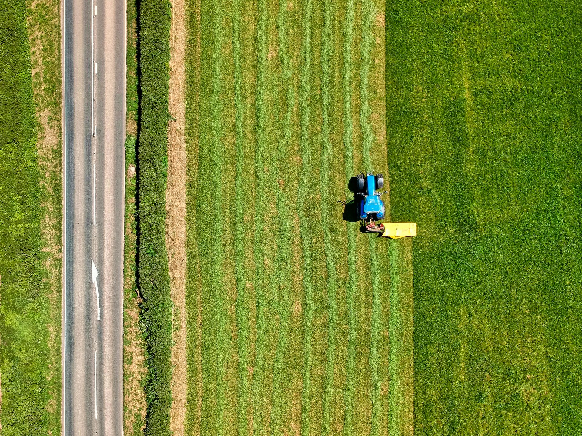 An aerial view of a tractor cutting grass next to a road.