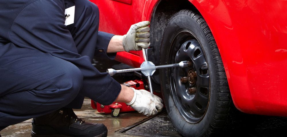 A Man Is Changing A Tire On A Red Car With A Tire Iron — Summit Smash In Polo Flat, NSW