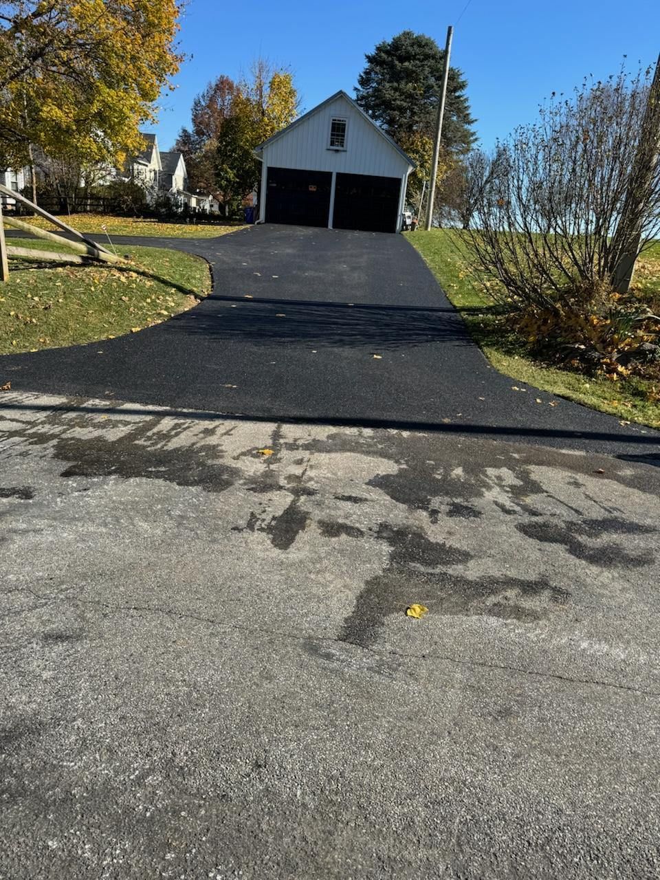 A driveway leading to a garage with a white house in the background.