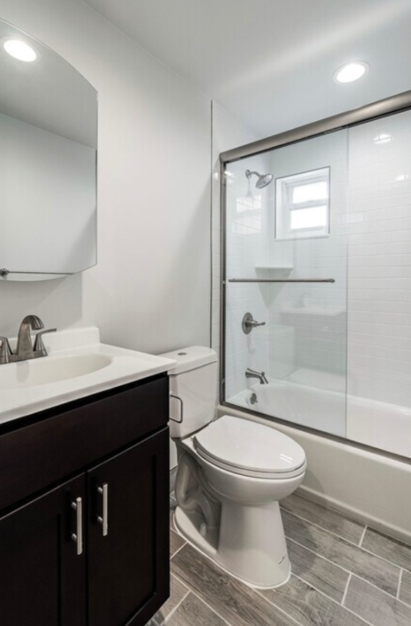 Bathroom with white walls, dark vanity, toilet, and glass shower door. Gray tile floor.