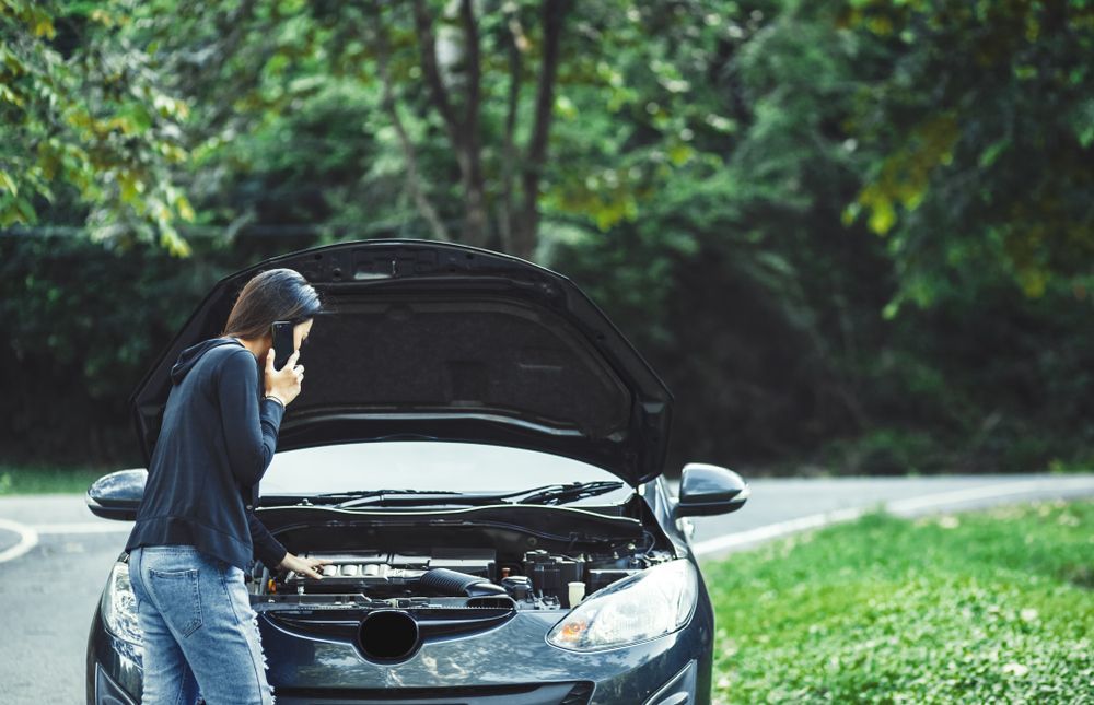 A Woman is Standing Next to a Broken Down Car Talking on a Cell Phone — 4off Automotive & Electrical In Bowral, NSW