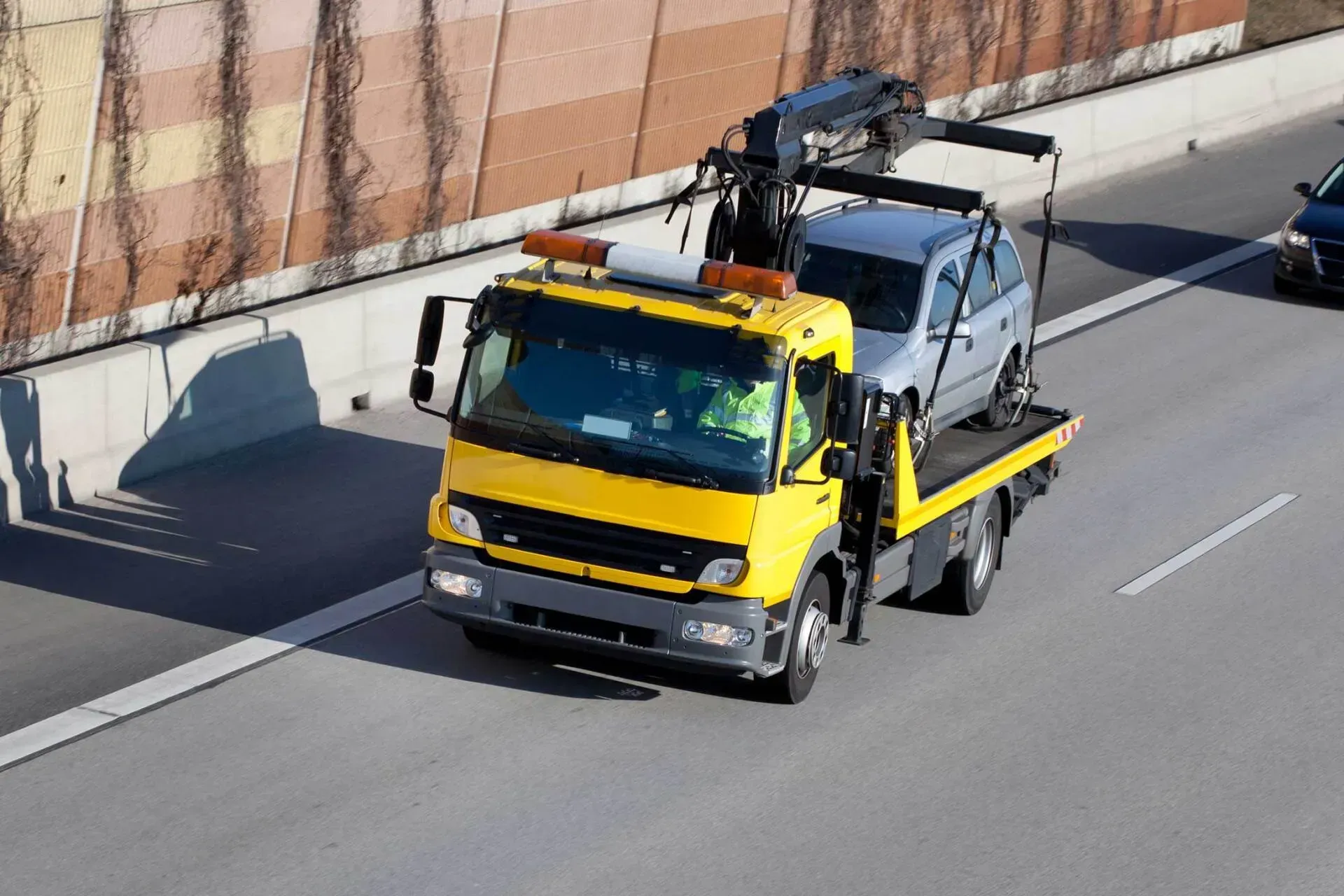 Yellow tow truck carrying a silver car on a highway.