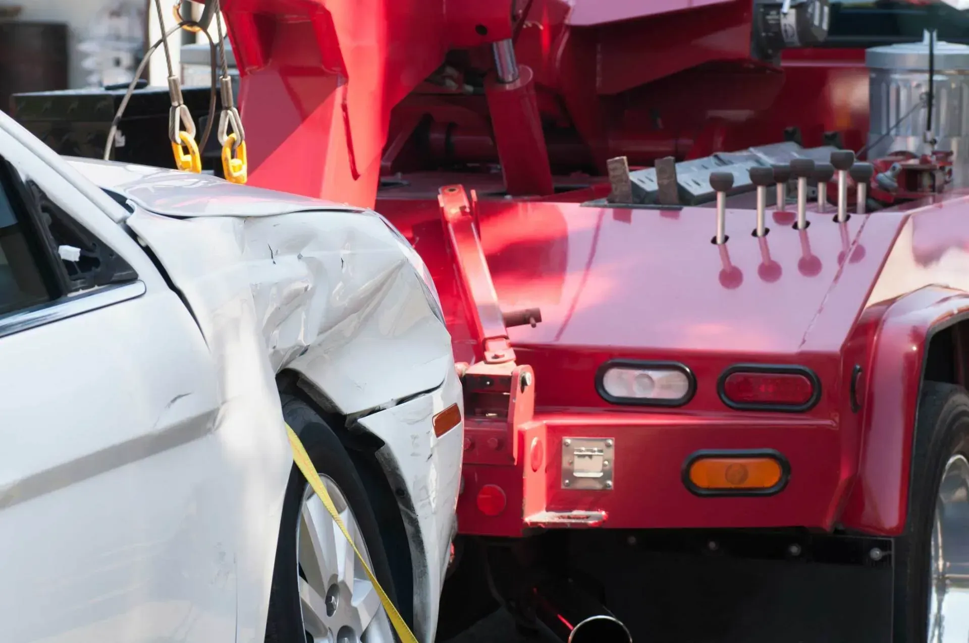 Damaged white car being towed by a red tow truck after an accident.