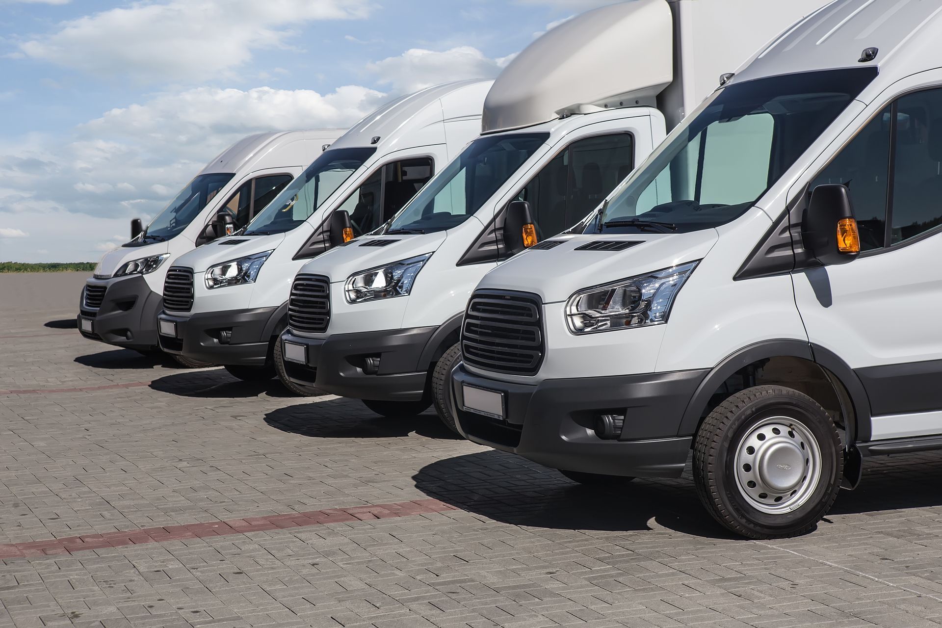 White delivery vans parked in a row on a paved surface under a cloudy sky.