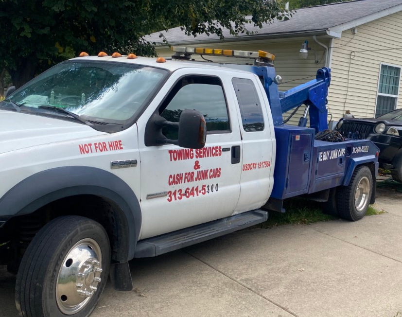 White tow truck with the phone number 313-478-5333 and the phrase “Cash for junk cars on the spot” against a black background.